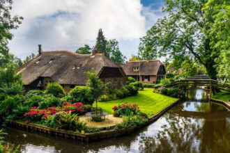 Πανόραμα του Giethoorn, ενός γραφικού ολλανδικού χωριού με κανάλια, ξύλινα γεφυράκια και σπίτια με αχυρένιες σκεπές, γνωστού ως η «Βενετία του Βορρά», κάτω από έναν γαλάζιο ουρανό.