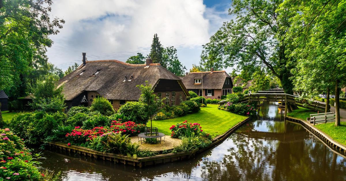 Πανόραμα του Giethoorn, ενός γραφικού ολλανδικού χωριού με κανάλια, ξύλινα γεφυράκια και σπίτια με αχυρένιες σκεπές, γνωστού ως η «Βενετία του Βορρά», κάτω από έναν γαλάζιο ουρανό.